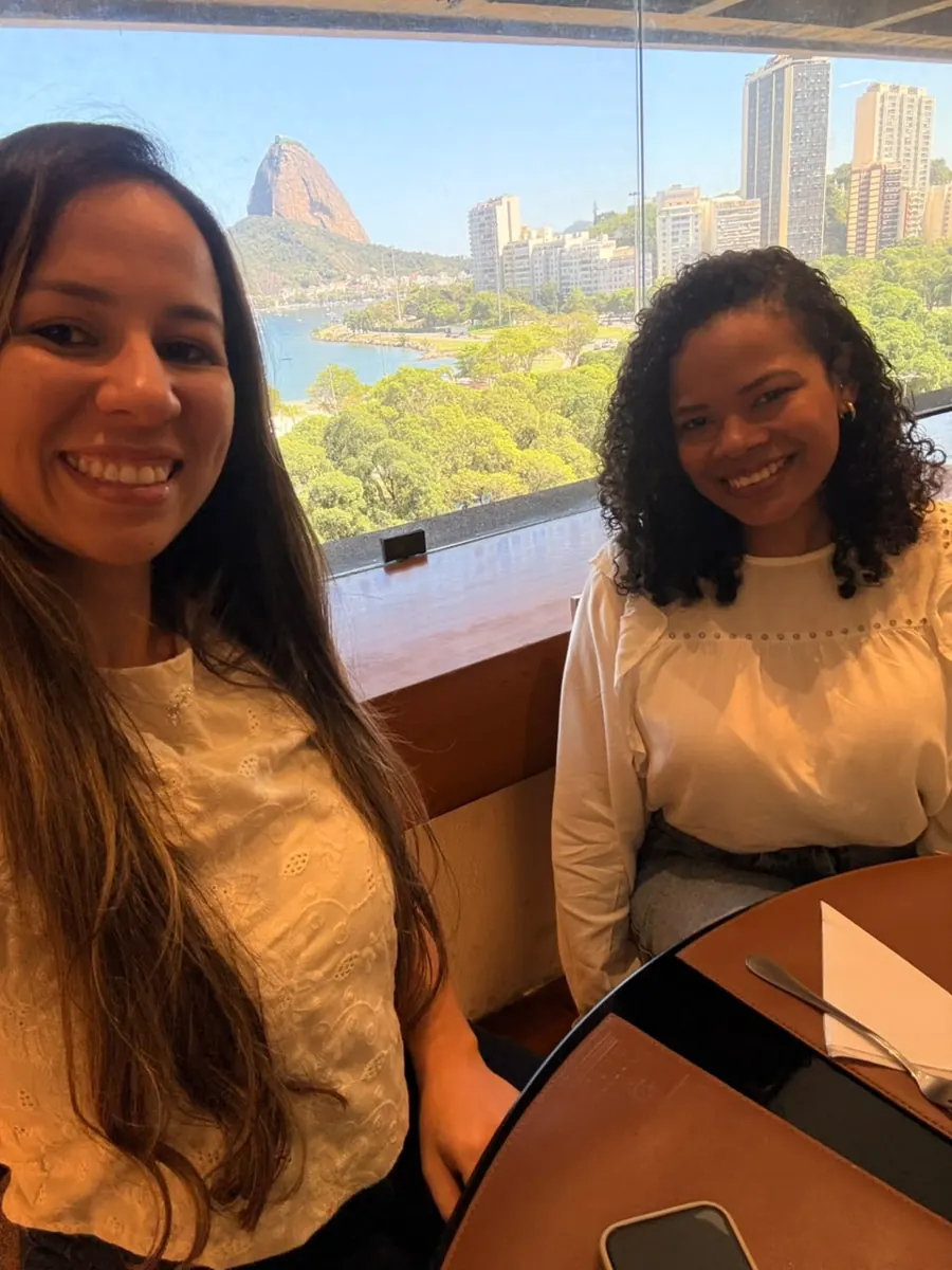 Anlive e Juliana, sócias da Viaje Bem, sorrindo com o Pão de Açúcar ao fundo